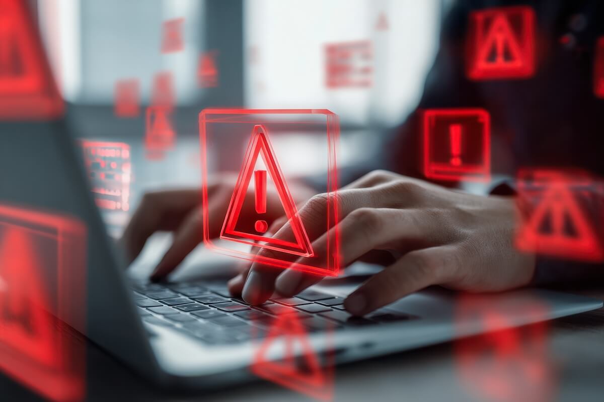Hands typing on a laptop keyboard with red digital warning icons layered over the screen.
