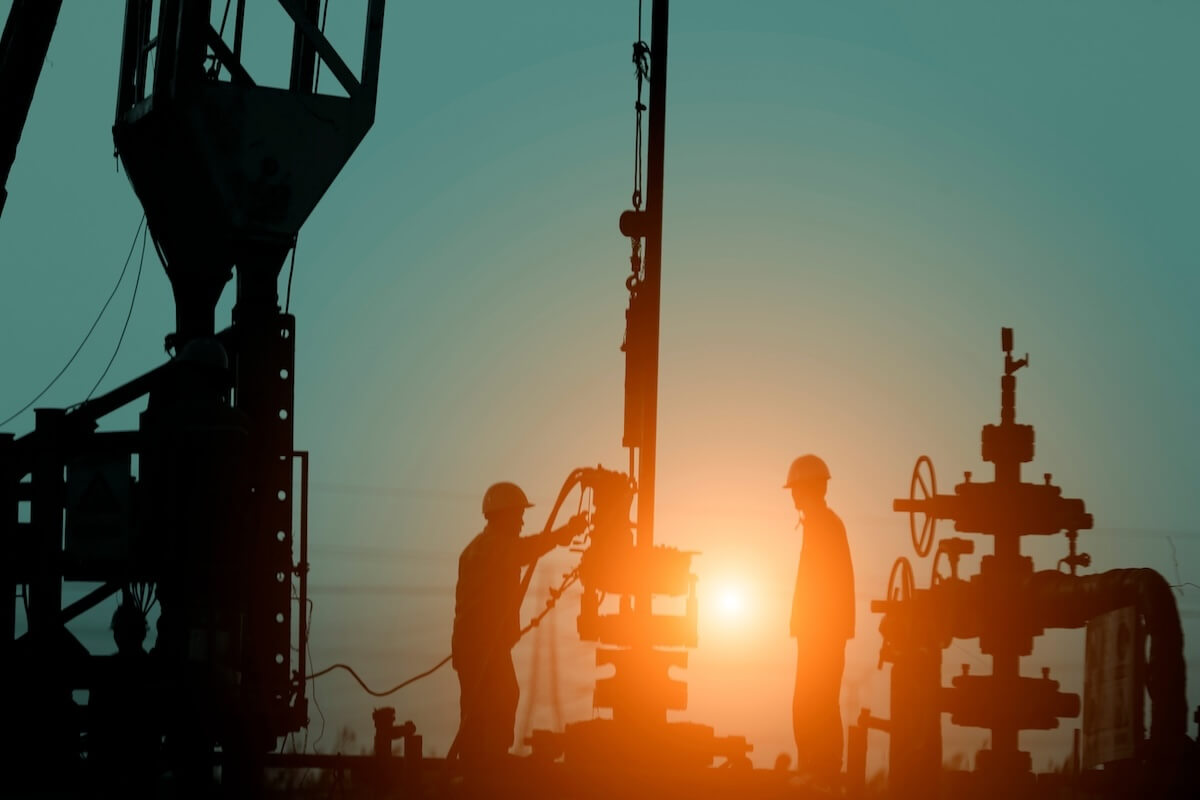 Silhouettes of oilfield workers and drilling equipment against a sunset in the Permian Basin.