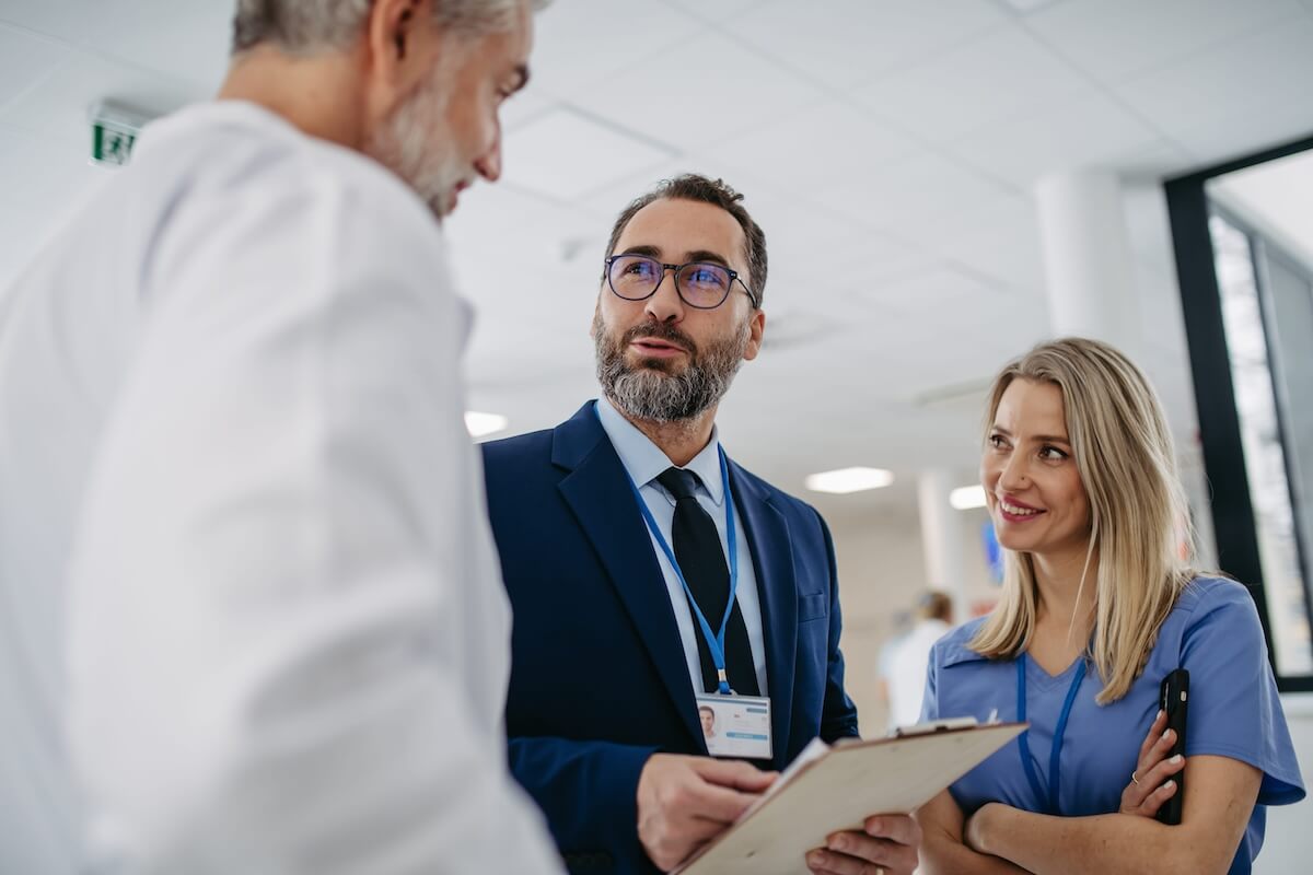 Man in suit holding clipboard and talking to a dentist and dental assistant in a clinic.
