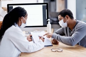 A medical professional and patient looking concerned while working on documents in a clinic.
