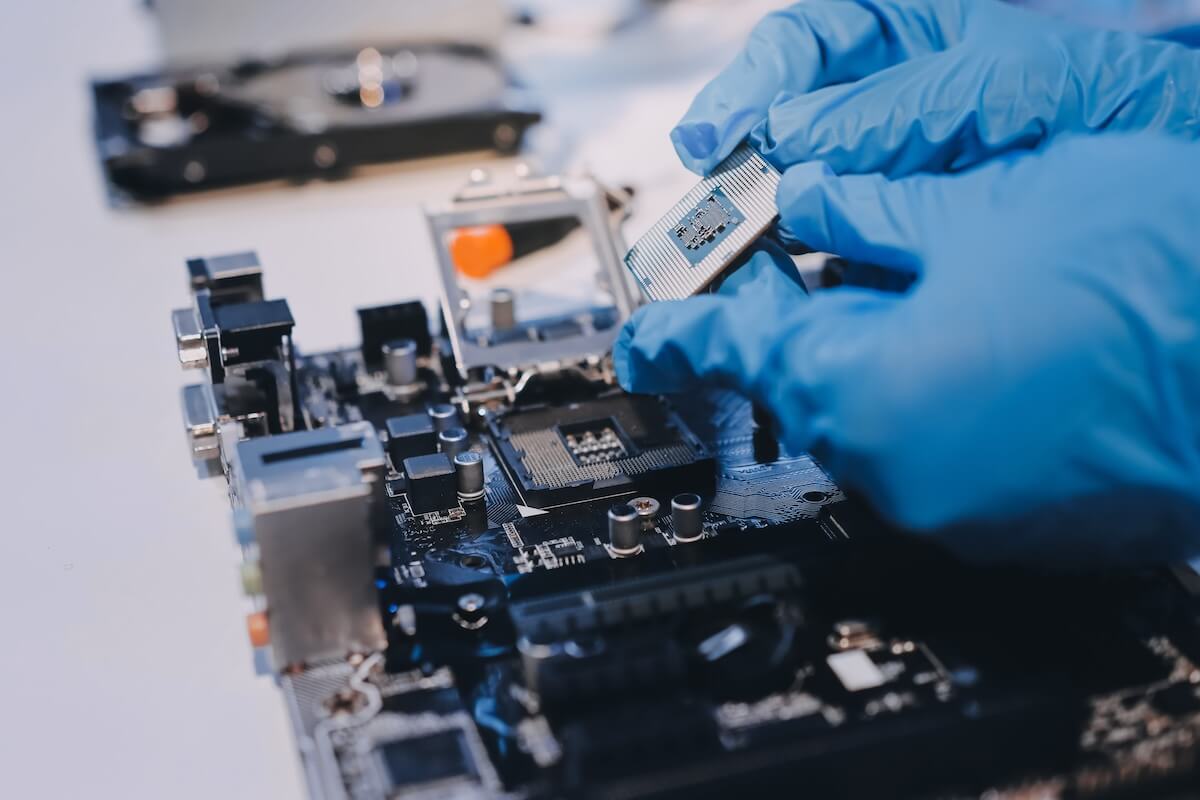 Gloved hands installing a silver computer processor chip onto a circuit board motherboard.