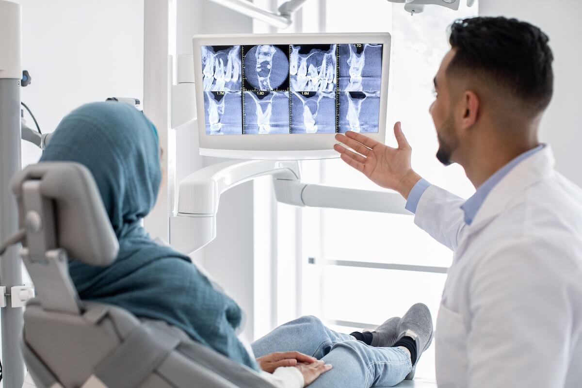 Male dentist showing digital x-ray scans on a monitor to a female patient wearing a hijab.