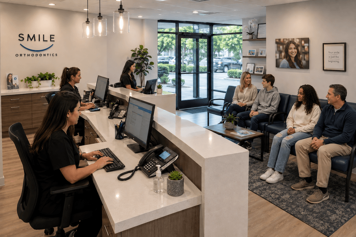 Receptionists working at computers in a busy orthodontics office front desk with patients in the waiting room.
