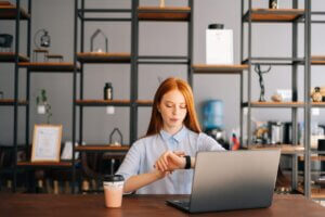 A professional woman checks her smartwatch at a modern office desk with a laptop, representing fast response time.