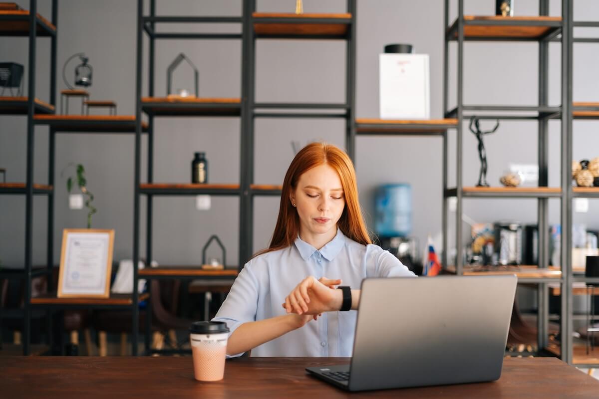 law-firm-efficient-it-response-time A professional woman checks her smartwatch at a modern office desk with a laptop, representing fast response time.