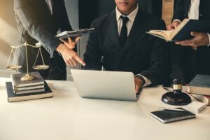 Legal professionals point to data on a laptop next to a gavel and scales of justice, illustrating operational accountability.