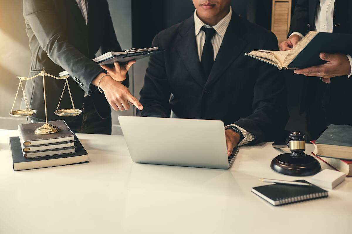 Lawyers in an Office Legal professionals point to data on a laptop next to a gavel and scales of justice, illustrating operational accountability.