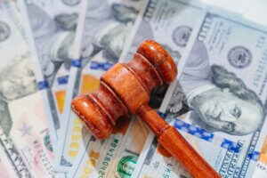 A wooden legal gavel rests on top of several scattered one-hundred-dollar bills, illustrating law firm IT costs.