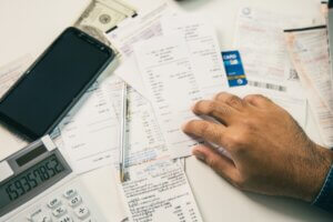 A person reviews a desk scattered with invoices, a calculator, and a smartphone, symbolizing legal cybersecurity budgeting.