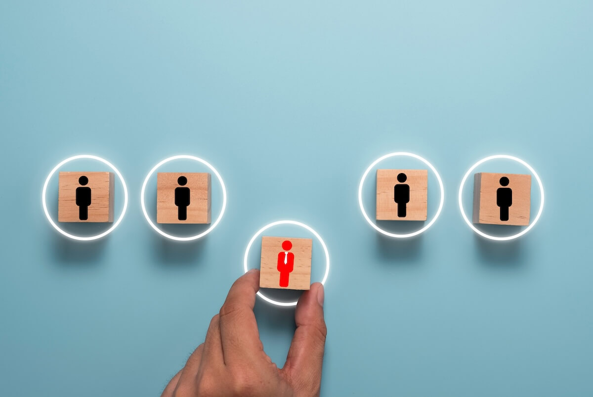 A hand selects a distinct red figure on a wooden block among black figures, illustrating vendor management delegation.