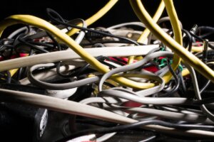 A messy, tangled cluster of yellow, white, and black ethernet cables and power cords representing unmanaged IT infrastructure.