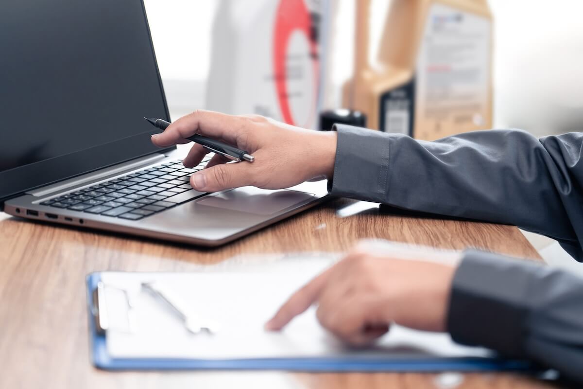 cyber-insurance-compliance-checklist Hands holding pen over laptop screen next to clipboard checklist at desk, reviewing compliance requirements.