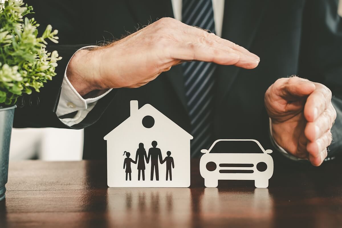 insurance-agency-it-provider-switch-protection Hands sheltering paper cutouts of a family, house, and car, representing security and insurance protection.