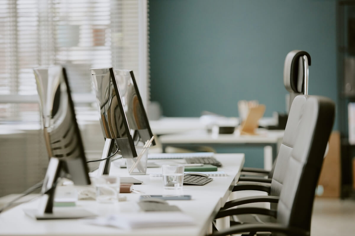 modern-cybersecurity-stack-insurance-agency Row of empty office computer workstations with monitors, keyboards, and office chairs along a white desk.