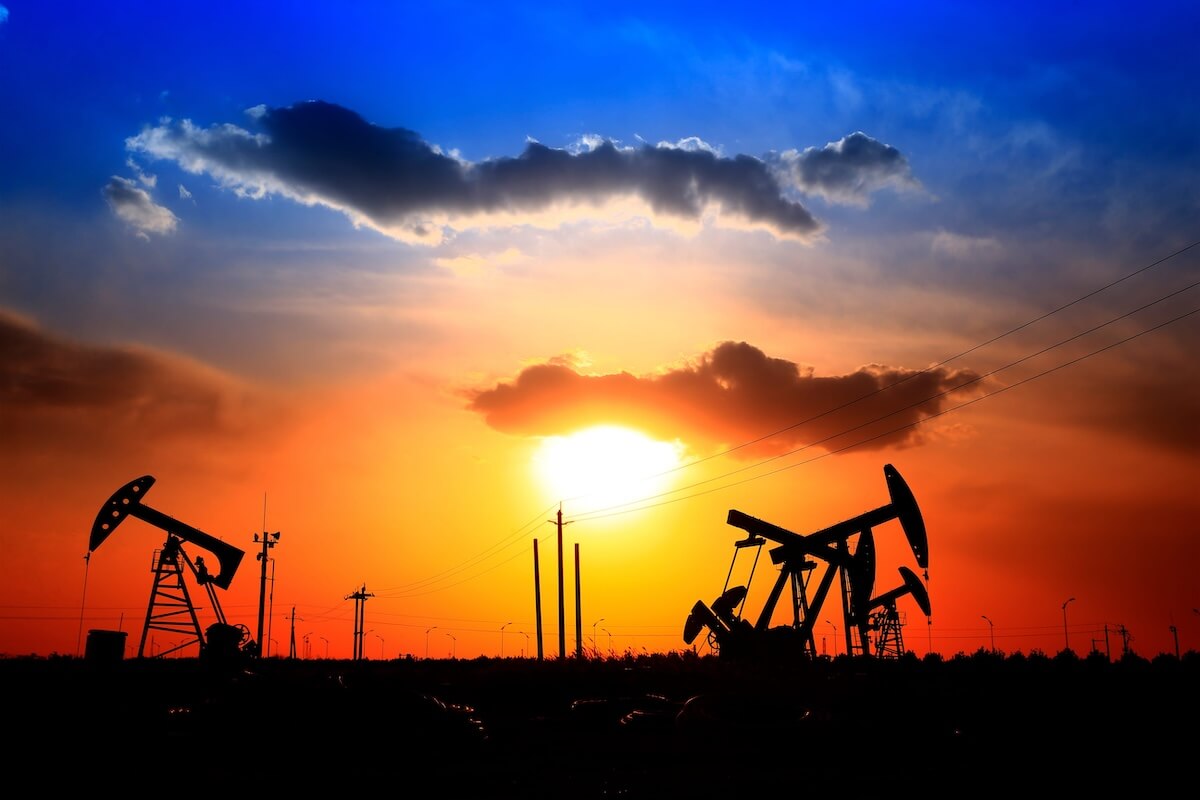 Silhouetted oil pump jacks operating against a vibrant orange and blue sunset sky in the Permian Basin.