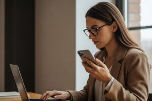 Business professional using a smartphone while working on a laptop.