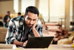 man in warehouse in plaid shirt dealing with a computer problem at work